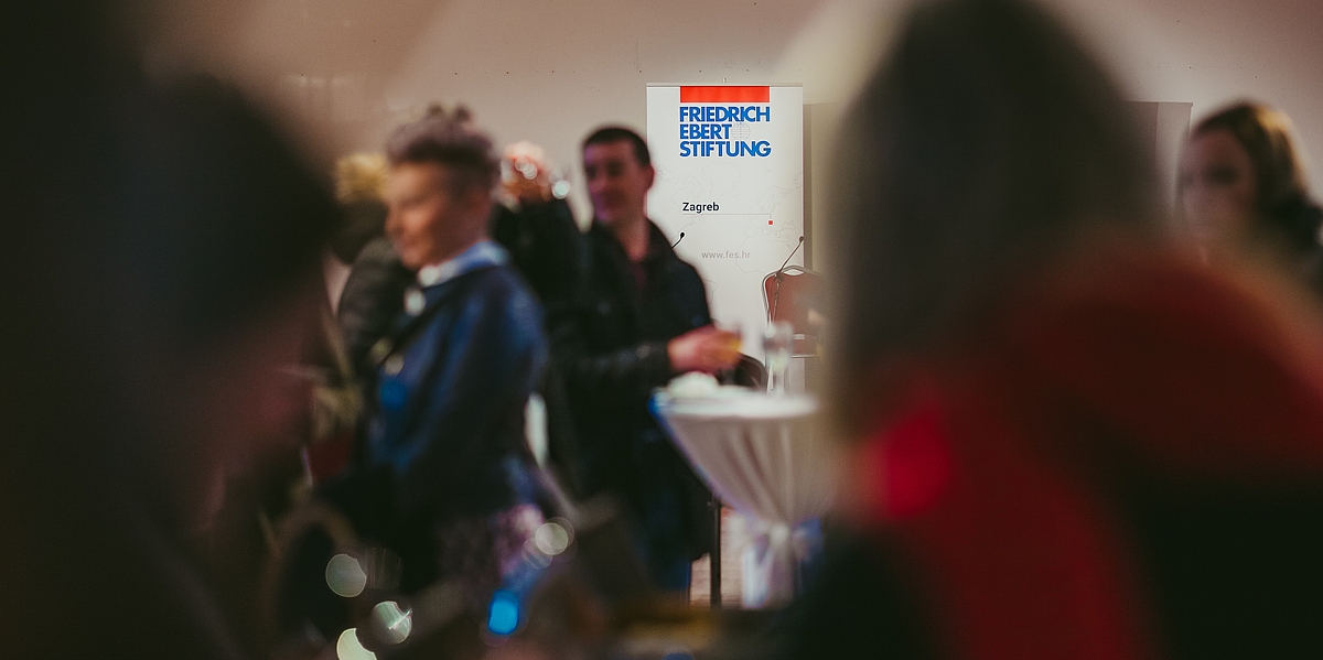 Fotografija događaja koji je organizirala Zaklada Friedrich Ebert, s velikom okupljenom publikom koja međusobno razgovara, te roll-up panoom s FES logom u pozadini.