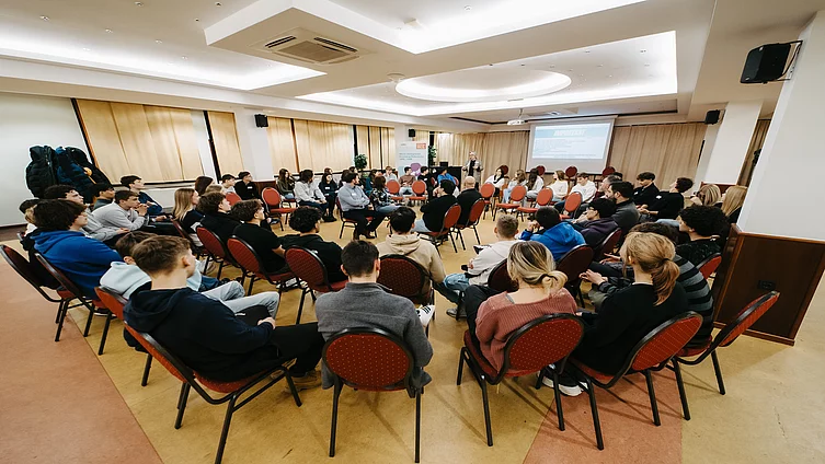 A large crowd of young people sitting in multiple circular seating arrangements for fishbowl method at an indoor event.