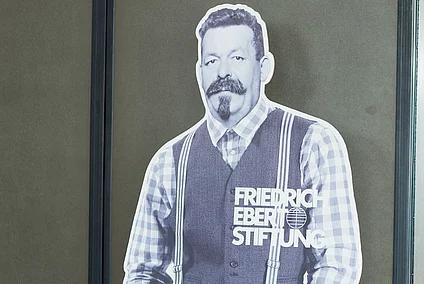 Fotografija bannera u obliku siluete Friedricha Eberta. U pozadini je vidljiva dvorana, panel rasprava, te publika na eventu Zaklade.