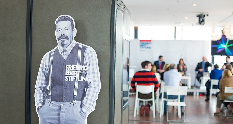 Fotografija bannera u obliku siluete Friedricha Eberta. U pozadini je vidljiva dvorana, panel rasprava, te publika na eventu Zaklade.