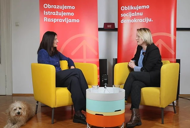 Fotografija snimateljskog studija tijekom vodcasta, s moderatorom i govornikom koji sjede u naslonjačima i gledaju jedan drugoga, dok se u pozadini nalaze dva crvena FES roll-upa, a pas odmara u donjem lijevom kutu.